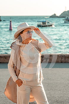 Happy blonde woman in a white suit and hat posing at the camera against the backdrop of the sea