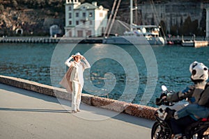 Happy blonde woman in a white suit and hat posing at the camera against the backdrop of the sea