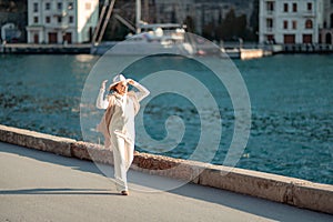 Happy blonde woman in a white suit and hat posing at the camera against the backdrop of the sea