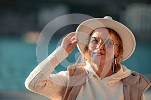 Happy blonde woman in a white suit and hat posing at the camera against the backdrop of the sea