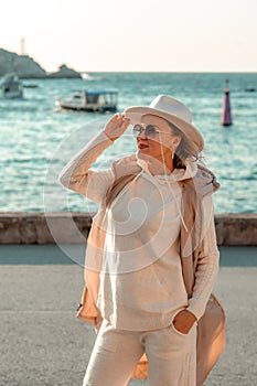 Happy blonde woman in a white suit and hat posing at the camera against the backdrop of the sea