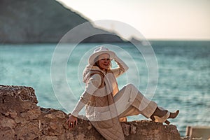 Happy blonde woman in a white suit and hat posing at the camera against the backdrop of the sea