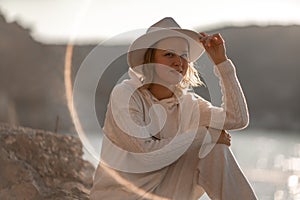 Happy blonde woman in a white suit and hat posing at the camera against the backdrop of the sea