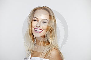 Happy blonde young woman with beautiful natural makeup and long wavy hair, with bare shoulders, over white background.