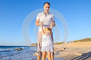 Happy blondy child girl with her father holding hands and having fun walking on the beach. Family vacation, travel concept. Bright