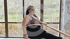 Happy body positive fat woman with dreadlocks doing stretching in the gym. Concept of natural diverse beauty and sport