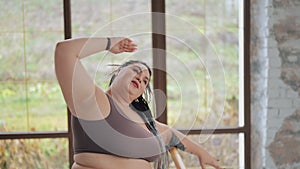 Happy body positive fat woman with dreadlocks doing stretching legs in the gym. Concept of natural diverse beauty and