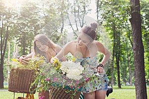 Happy boho chic girls gather wild flowers on bicycle ride