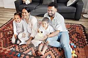 Happy, bonding family quality time at home with parents watching a movie and having snacks on the floor. Young couple