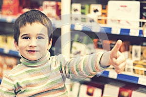 Happy boy 4 years in a supermarket on the background of shelves with chocolate. The boy showed that everything is ok. toned