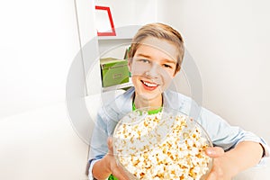 Happy boy with big popcorn bowl on white sofa