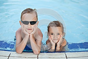 Happy boy with blond hair and little girl smiling sitting in swimming pool