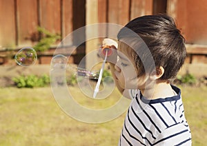 Happy boy blowing soap bubbles in the garden, Cute 4 years old kid blowing bubble wand with a funny face, Active kid playing in
