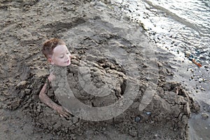 Happy boy buried in sand on beach