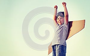 Happy boy with cardboard boxes of wings against sky dream of fly