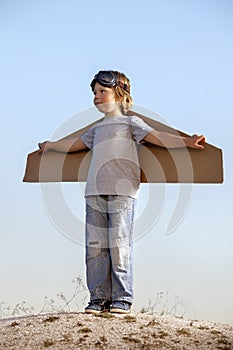 Happy boy with cardboard boxes of wings against sky dream of fly