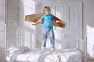 Happy boy with cardboard boxes of wings in home dream of flying