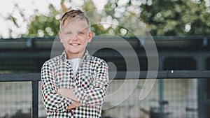 happy boy in checkered shirt standing with crossed arms and smiling at camera photo