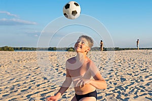 Happy boy cheerfully plays football on the beach, on a sunny day. Outdoor sports games. Active healthy lifestyle concept