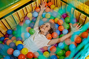 Happy boy child playing in basin filled with multi colored plastic ball