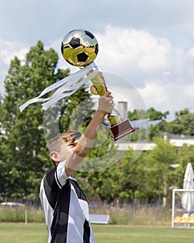 Happy boy child soccer player champion in football championship with trophy gold cup with golden football ball