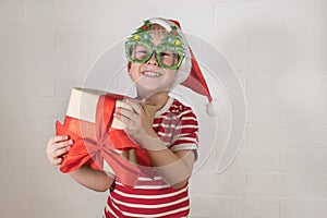 A happy boy in a Christmas costume and carnival glasses holds a gift in his hands.