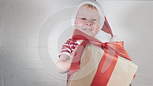 A happy boy in a Christmas outfit receives a gift, a box with a red ribbon.