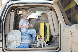 Happy boy in a cowboy hat and puppy jack russell terrier travel by car. A child and a funny little dog are sitting in