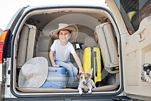 Happy boy in a cowboy hat and puppy jack russell terrier travel by car. A child and a funny little dog are sitting in