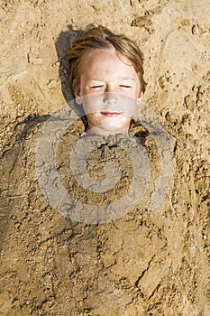 Happy boy dig oneself in the sand