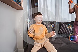 Happy boy with down syndrome rejoicing while his mother blowing soap bubbles