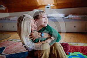 Happy boy with Down syndrome sitting on floor and hugging with his grandmother at home