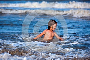 Happy boy enjoys life on summer beach. Cute kid having fun on sandy beach in summer. Ocean or sea wawes on the photo