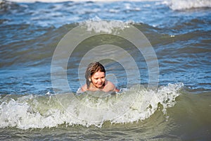 Happy boy enjoys life on summer beach. Little boy in the spray of waves at sea on a sunny day. Ocean or sea wawes on the photo