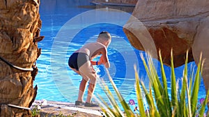 Happy boy in flippers jumping into the blue water pool. Slow motion