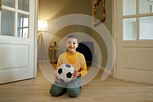 Happy boy football fan posing for camera with soccer ball at home