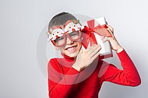 Happy boy Gen Alpha in a red christmas holidays sweater and funny party glasses. Stylish boy with a Christmas gift have