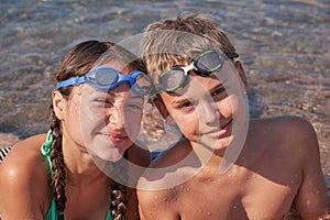 Happy boy and girl in goggles lie in the sea on shore. Portrait of children looking at the camera.