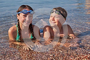 Happy boy and girl in goggles lie in the sea on shore. Portrait of children looking at the camera.