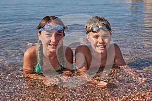 Happy boy and girl in goggles lie in the sea on shore. Portrait of children looking at the camera.