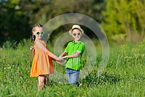 Happy boy and girl holding hands playing on a meadow in sunny day