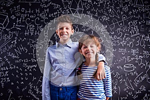 Happy boy and girl at school against big blackboard.