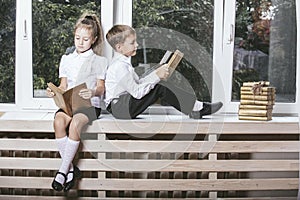 Happy boy and girl sitting on the windowsill reading books on th