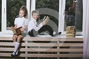 Happy boy and girl sitting on the windowsill reading books on th