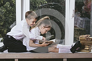 Happy boy and girl sitting on the windowsill reading books on th