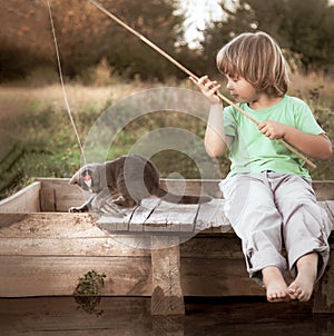 Happy boy go fishing on the river with pet, one children and kitten of the fisherman with a fishing rod on the shore of the lake