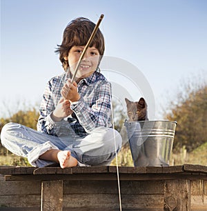 Happy boy go fishing on the river with pet, one children and kitten of the fisherman with a fishing rod on the shore of the lake