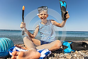 Boy has water polo ball and scuba gear on the beach. Looking at camera. Concept of travel, tourism, family