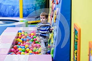 Happy boy having fun in ball pit in kids amusement park and indoor play center. Child playing with colorful balls in playground