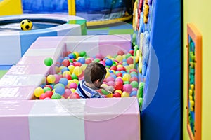 Happy boy having fun in ball pit in kids amusement park and indoor play center. Child playing with colorful balls in playground